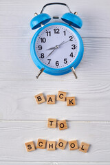 Back to school concept. Blue alarm clock on white wood.