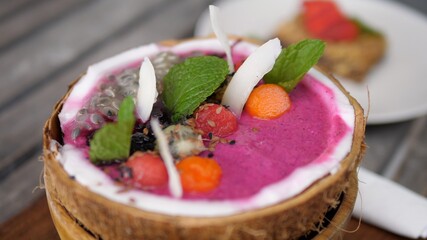 Breakfast on holidays. Detailed view of tropical smoothie served in coconut bowl with muesli and a glass of coffee. 