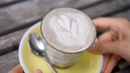 Hands taking away a glass of dairy free cappuccino with hearty art foam. 