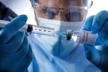 Medico con mascherina chirurgica e guanti in lattice preleva il vaccino anti-covid da una fiala di...