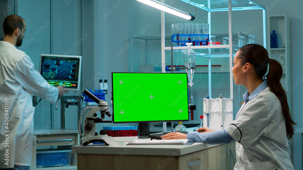 Wall mural biochemist sitting at workplace in laboratory using green mock-up screen personal computer with chro