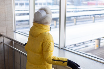 Young woman at the railway station in a protective mask on the face in winter clothes passenger