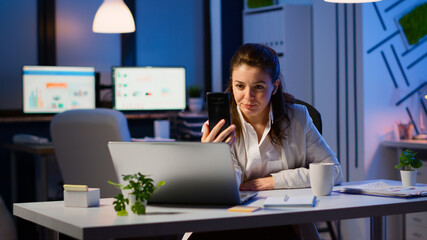 Business woman discussing during video conference with partners using smartphone and headphone late...