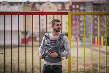 Handsome young father with baby carrier outdoors 