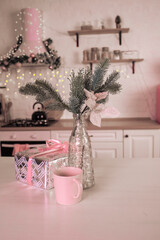 composition in pink tones from a vase with a spruce branch, a cup and a New Year's gift, against the background of a decorated kitchen