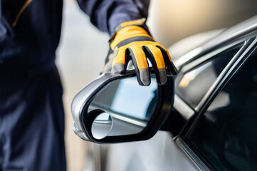 Male auto mechanic hand wearing yellow glove adjusting car wing mirror. Checking car part in...