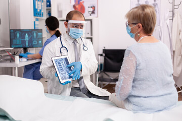 Healthcare physician wearing face mask as safety precaution showing x-ray on tablet pc in time of covid19. Medical physician specialist during coronavirus outbreak discussing with patient.