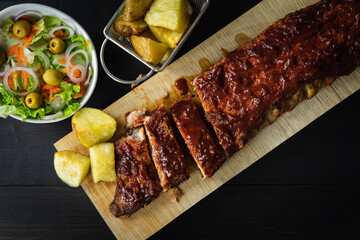 Barbecue ribs and potatoes on a wooden board. Coy space.