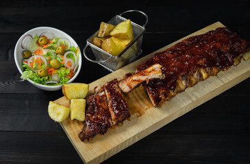 Barbecue ribs and potatoes on a wooden board. Coy space.