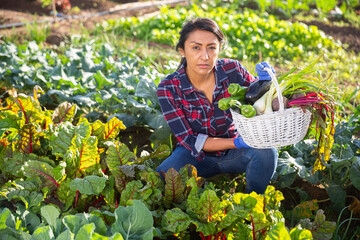 Fototapeta premium Smiling hispanic female gardener holding fresh greens and vegetables grown in her home garden