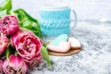 Bouquet of pink tulips, a cup of tea, and sweet gingerbread cookies in the shape of a heart on a light background. Copy space. Spring holiday concept, Valentine's Day.