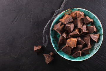 Organic chocolate pieces in a vintage bowl on a dark textured background, top view, copy space. Confectionery chocolate background.
