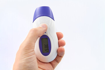 A man holding in his hand an electronic non-contact thermometer showing high temperature on white...