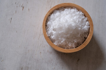 Fototapeta na wymiar Flower of salt, is a salt that forms as a thin, delicate crust on the surface of seawater in the wooden bowl on white wooden background. Selective focus. 