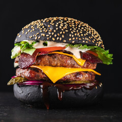 Big black burger grilled with double meat cutlet on a black background. Close up of black tasty...