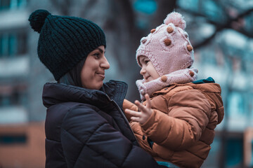 Young mother and cute girl child outdoors portrait. Winter photo. Cold outside people with winter hats