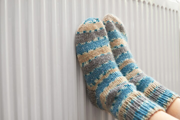 A girl in blue woolen socks warms her feet on the radiator