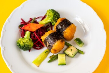 Fried roll with seaweed stuffed with rice, vegetable salad on white plate on yellow.
