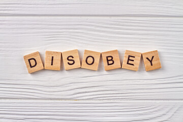 Abstract concept of disobey. Refusal to follow orders. Letters on wooden cubes isolated on wooden background.