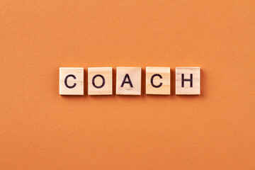 Coach is a specialist who is engaged in mentoring. Inspiration and motivation for business. Letters on wooden cubes isolated on orange background.