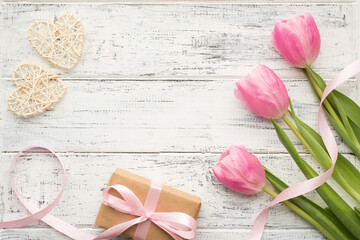 Happy valentines day concept. Flat lay overhead close up composition photo of pastel tulips with green stems kraft wrapped package and white hearts on wooden vintage desk