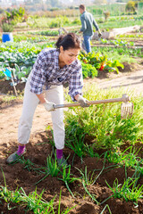 Woman of asian appearance working in garden between beds with hoe in hands