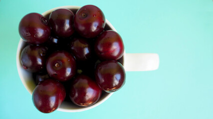 red juicy cherry in a white cup on a blue background top view . ripe summer berries