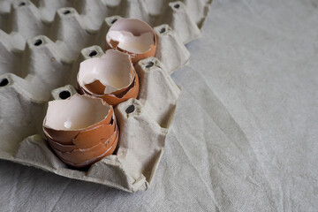 the shells of three broken eggs lie in a cardboard egg box lying on a gray cloth side view