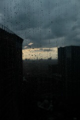 Rain drops on window with dark city and sunset view.