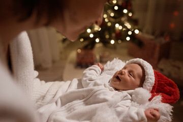 Happy young mother posing with newborn son under Christmas tree. High quality photo