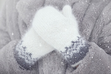 women's hands in hand-knitted down mittens with a pattern on the background of a faux fur coat