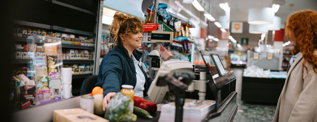 Cashier assisting customer at supermarket checkout - obrazy, fototapety, plakaty