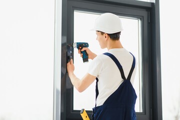 Workman in overalls installing or adjusting plastic windows in the living room at home