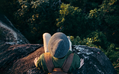 Asian teenager sitting on cliff bridge edge and looking at the mountain.