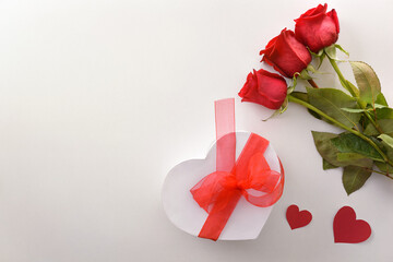 Red roses and gift with red bow on white top.