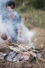 Fisherman placing fresh fish on bamboo stick for cooking on a fire
