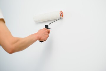 The painter is painting a wall in a room with a roller.