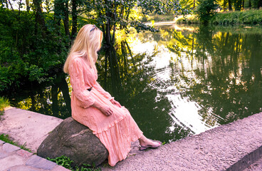 Sexy stunning blonde sitting by the river in a pink dress