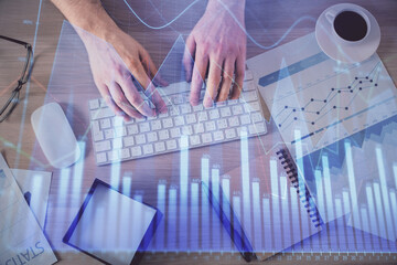 Multi exposure of man's hands typing over computer keyboard and forex graph hologram drawing. Top view. Financial markets concept.