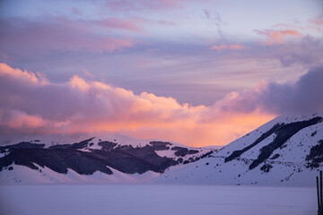 Winter sunset on the plain of castelluccio di norcia, in italy. The plain is covered with snow that reaches up to the fence. The warm sunset are reflected in the snow together with the colored clouds.