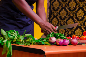 African chef carefully cutting vegetables with knife on the table