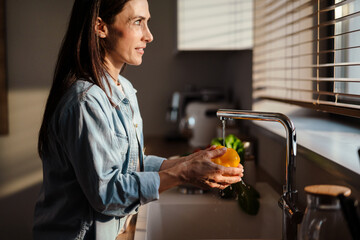 Smiling young woman washing vegetable in the sink