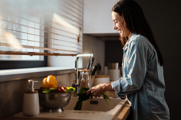 Smiling young woman washing vegetable in the sink