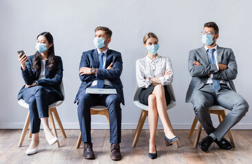 Multicultural business people in medical masks with devices waiting job interview in hall