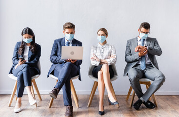 Multiethnic businesspeople in medical masks using devices before job interview