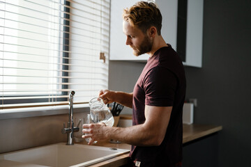 Attractive young man pouring water from a juf in a glass