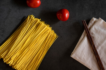 Yellow spaghetti and tomatoes on a black marble table. Yellow Italian Pasta. Raw spaghetti. Italian concept and menu