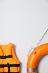 Orange life jacket, lifebuoy and space for text on light background. Rescue equipment