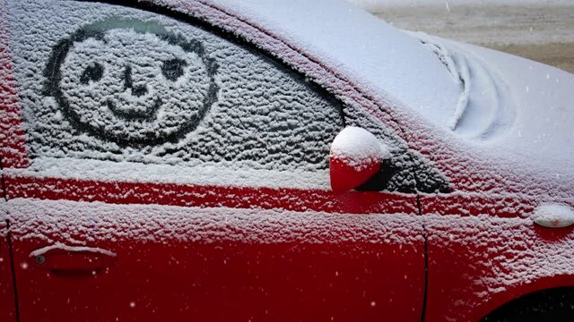 Snow covered car and a smiley figure writen on window