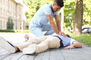 Passerby performing CPR on unconscious young man outdoors. First aid - obrazy, fototapety, plakaty